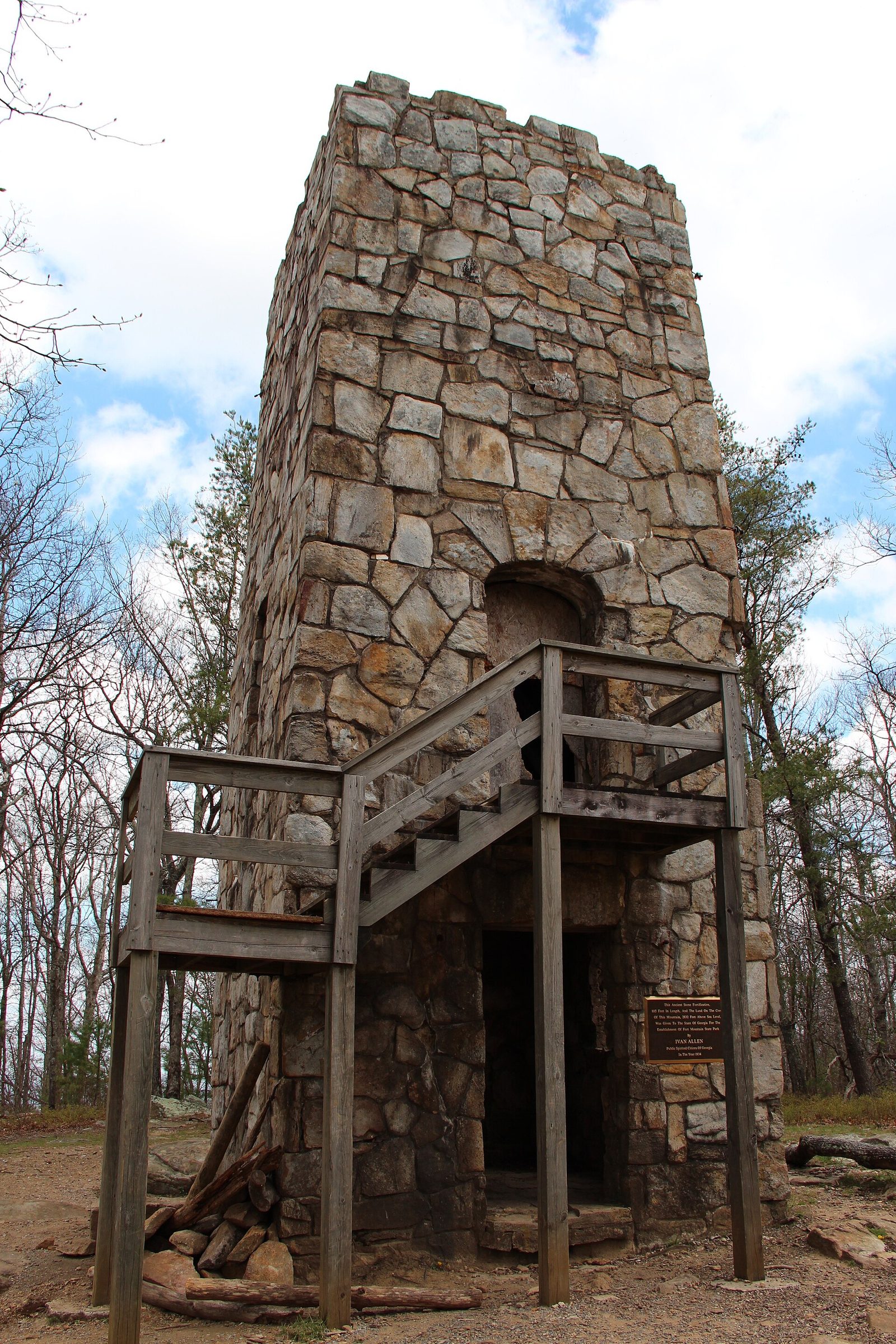 The tall crenellated stone fire tower at Fort Mountain State Park in Georgia, with a wooden staircase and platform at its arched doorway and bare winter trees around it