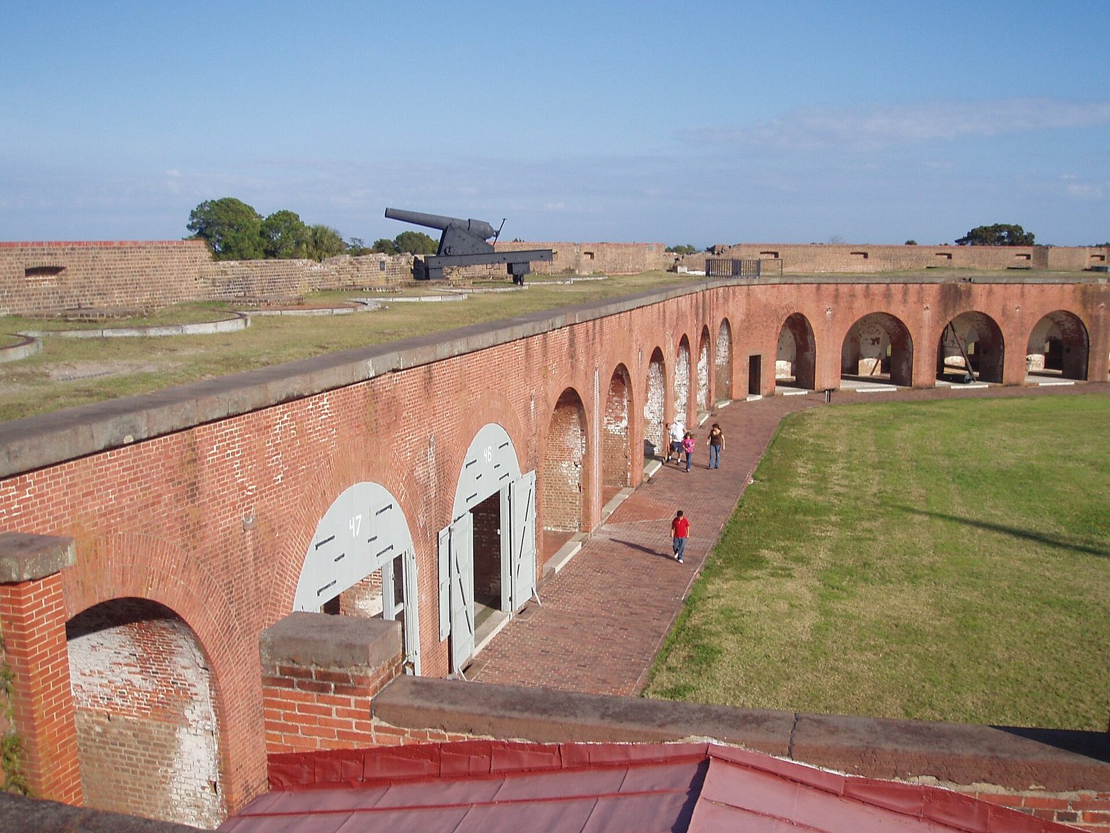 The brick casemate arches and grassed parade ground inside Fort Pulaski National Monument near Savannah, Georgia, with a cannon on the rampart above