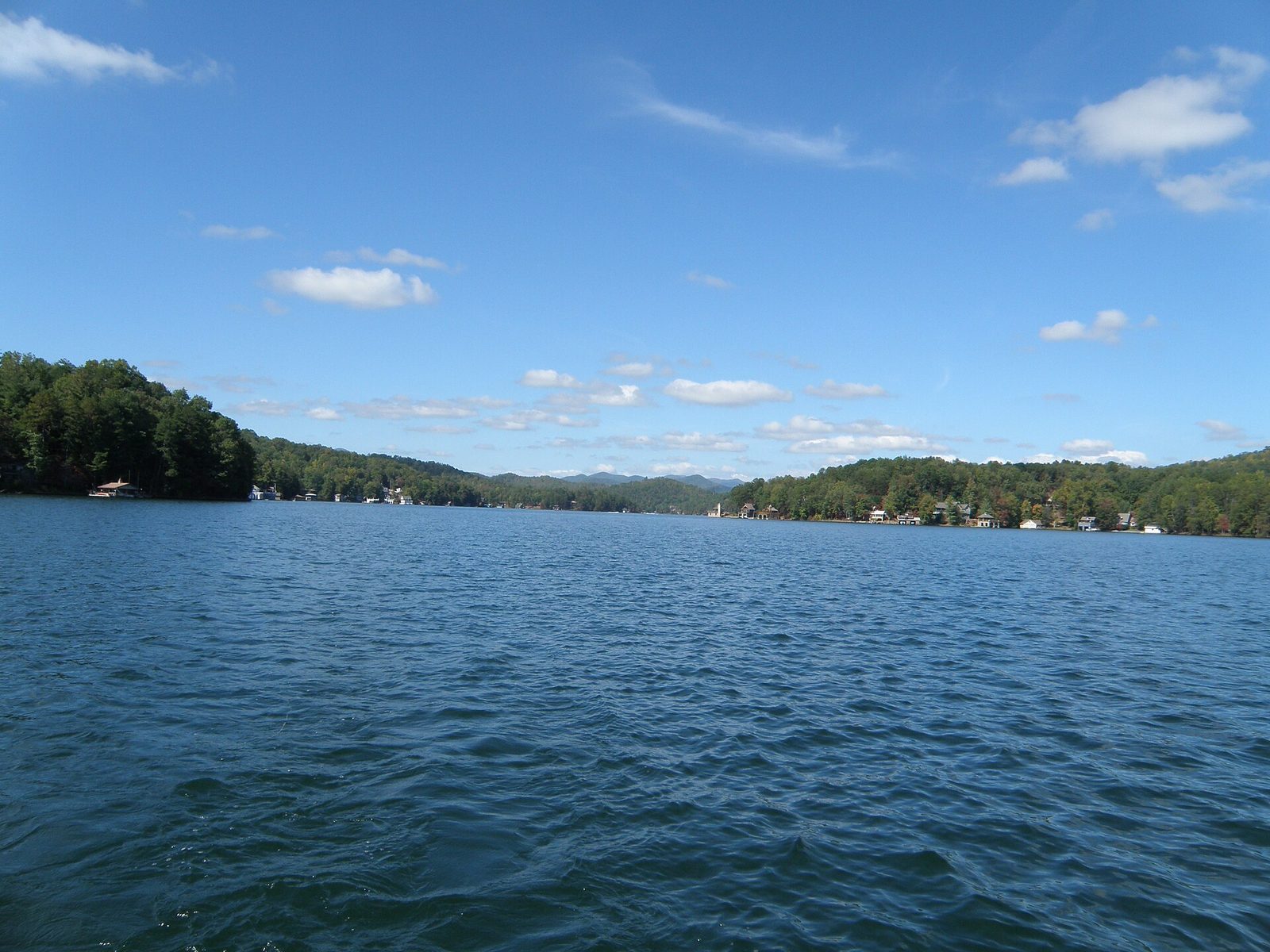 Lake Burton in Rabun County, Georgia, seen from the water, with wooded shores, boathouses and blue ridges beyond under a bright sky