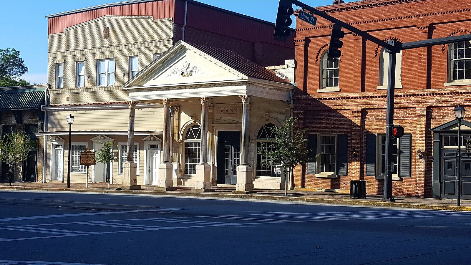 A columned classical-revival bank building and red brick storefronts on North Main Street in Madison, Georgia, in morning light