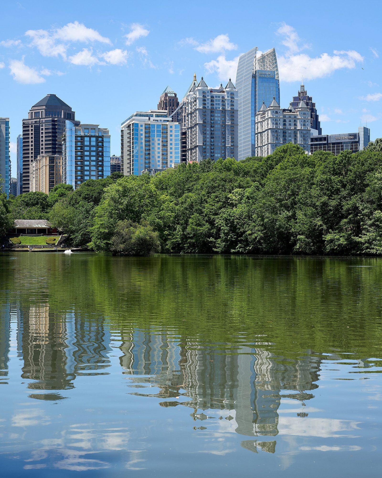 Lake Clara Meer in Piedmont Park, Atlanta, reflecting the Midtown skyline under a blue sky with scattered cumulus clouds in early May