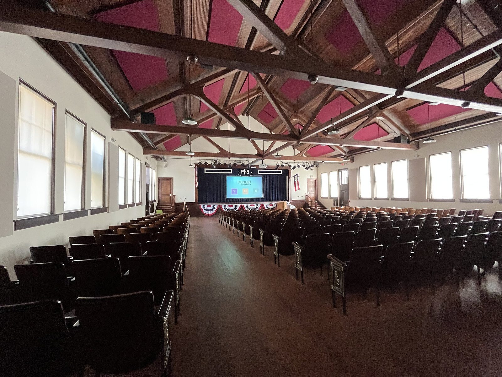 The restored auditorium inside the former Plains High School in Plains, Georgia, with rows of wooden seats facing a stage draped in red, white and blue bunting