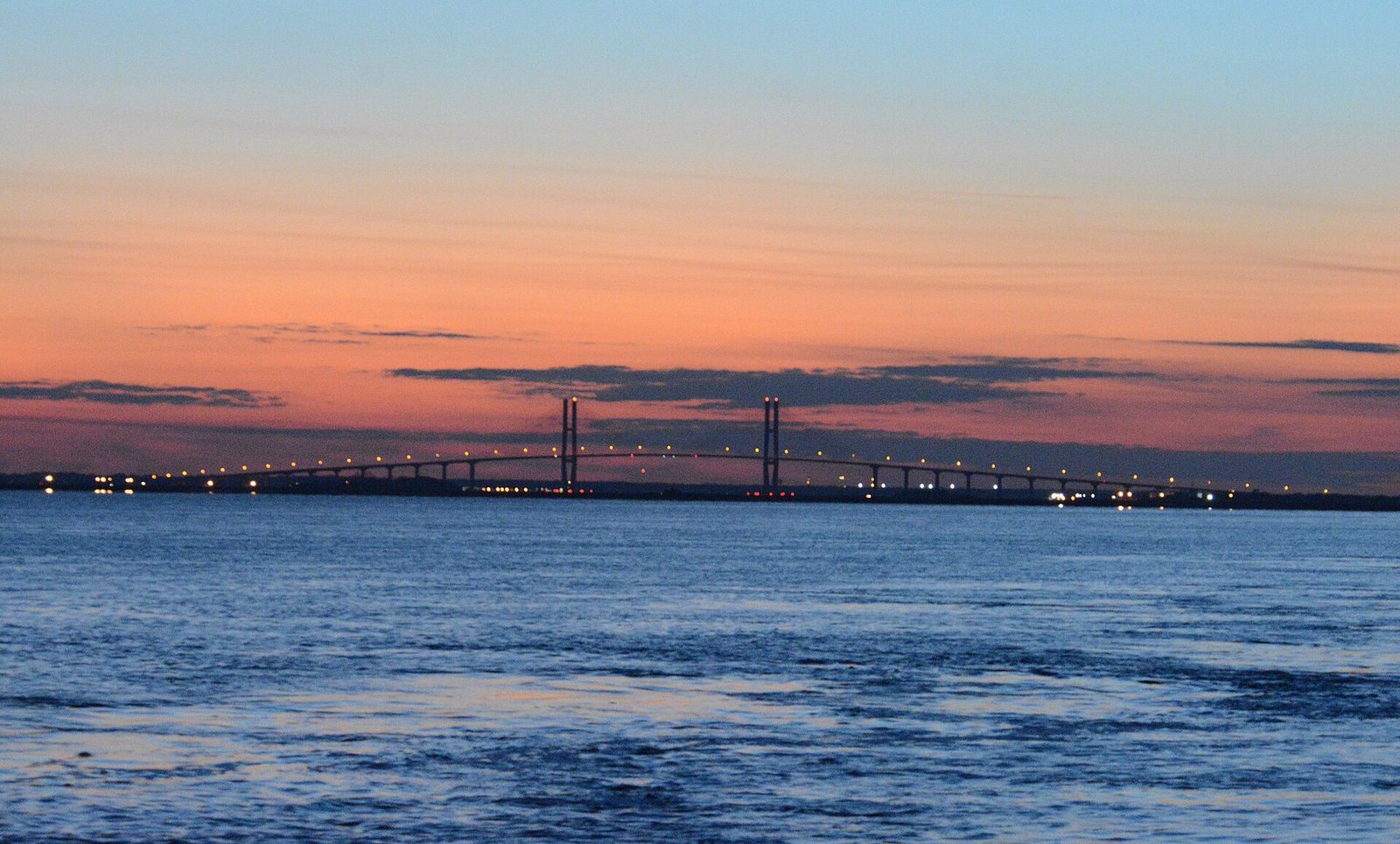The Sidney Lanier Bridge lit at dusk, its cable-stayed towers silhouetted against an orange and blue sky above the Brunswick River
