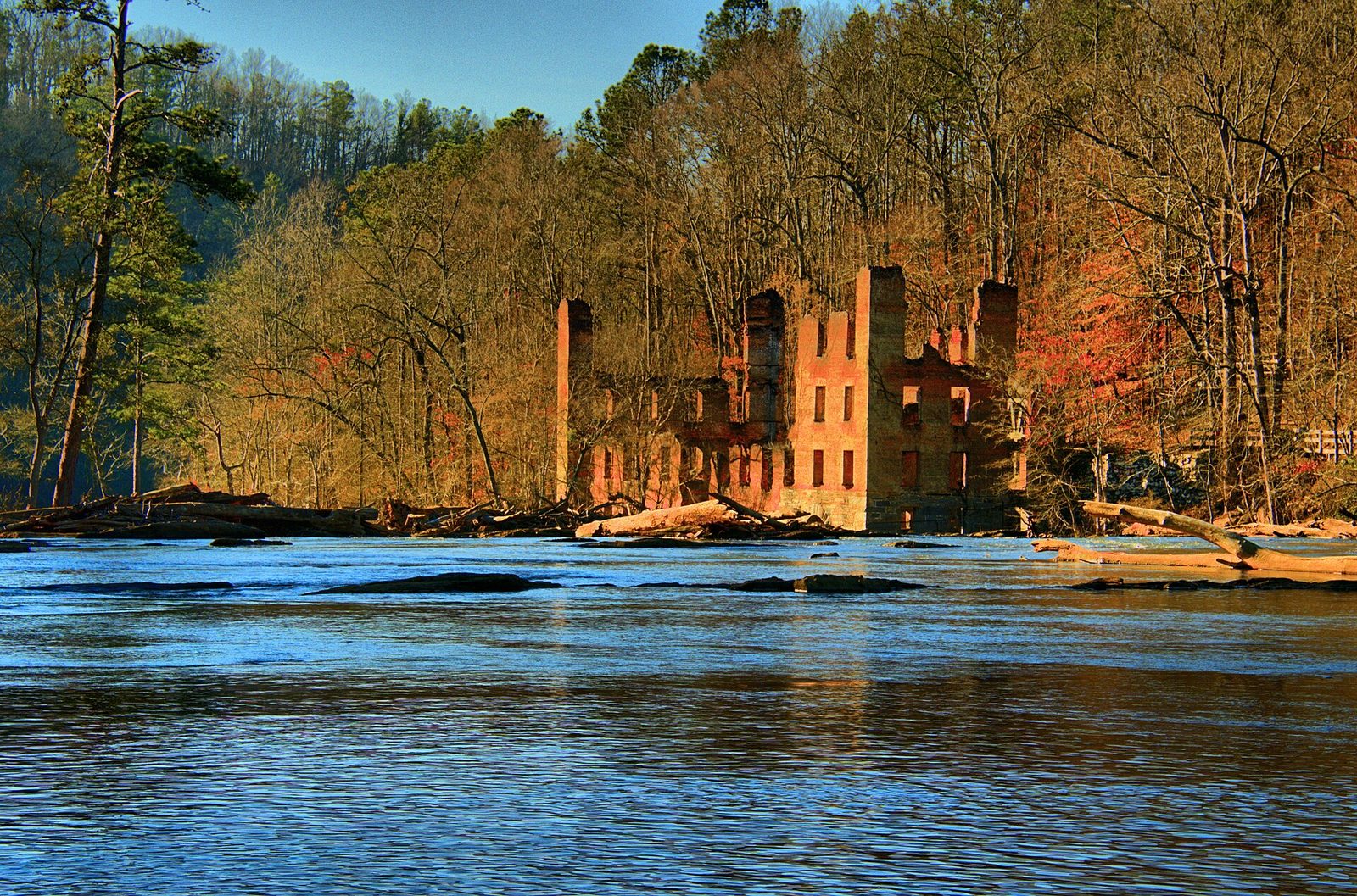 The roofless red brick shell of the New Manchester mill standing among bare winter trees across the water at Sweetwater Creek State Park