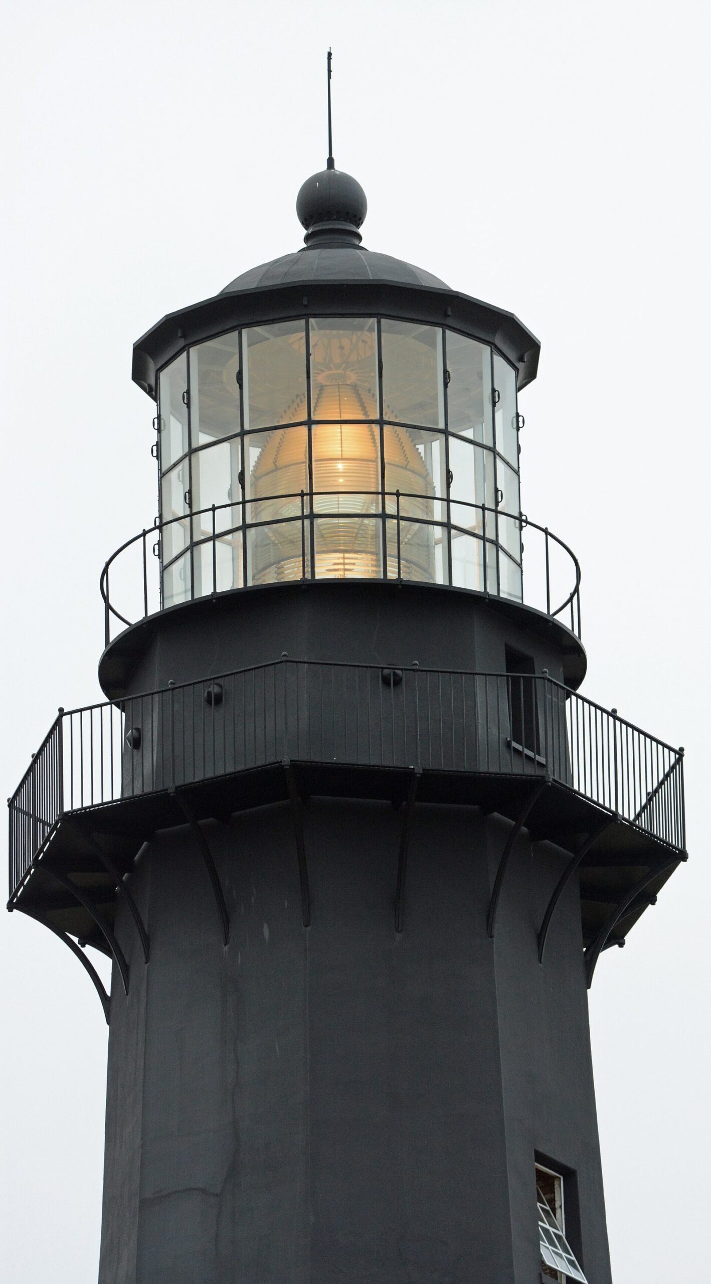 The black lantern room and gallery of the Tybee Island Light Station with its Fresnel lens lit against an overcast sky